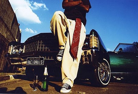 Capa do álbum do Racionais MC's: um homem apoiado num carro com a placa Racionais, de all-star e uma bandana vermelha pendurada na calça
